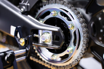 Close-up of the motorcycle wheel assembly, swingarm sprocket, and rear drive chain that powers the...