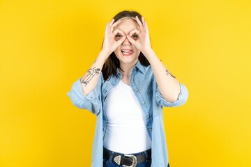 Beautiful woman wearing casual clothes doing ok gesture like binoculars sticking tongue out, eyes...