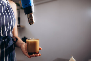 a woman dries wax and a newly filled candle with a hair dryer