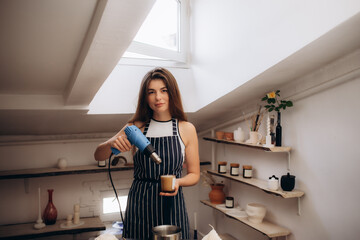 Production of candles. A woman dries wax with a hair dryer