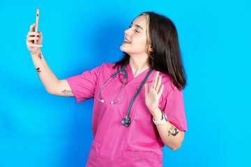Young caucasian doctor woman wearing pink medical uniform smiling and taking a selfie ready to post...
