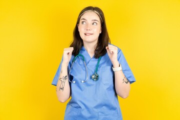 Young caucasian doctor woman wearing blue medical uniform clenches fists and awaits for something...