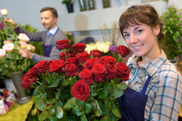 female florist holding glass vase with roses in flower shop