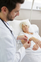 Fototapeta premium doctor securing identification tag on senior female patient in hospital