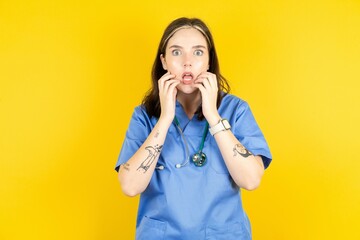 Speechless Young caucasian doctor woman wearing blue medical uniform keeps hands near opened mouth...