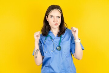 Irritated Young caucasian doctor woman wearing blue medical uniform blows cheeks with anger and...