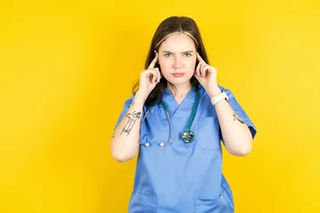 Fotobehang Serious concentrated Young caucasian doctor woman wearing blue medical uniform keeps fingers on temples, tries to ease tension, gather with thoughts and remember important information for exam © Roquillo