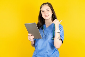 Young caucasian doctor woman wearing blue medical uniform pointing empty space modern device