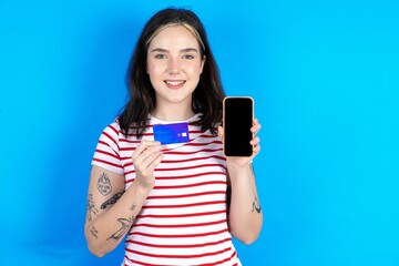 Photo of adorable beautiful young woman wearing striped T-shirt holding credit card and Smartphone. Reserved for online purchases