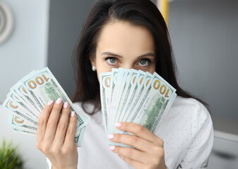 Woman holds one hundred dollar bills at face level and looks at camera. Earnings for women concept