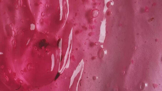 Liquid drops of transparent pink cosmetic sample texture with bubbles  flowing on the pink surface. Macro shot of peeling gel with raspberry dripping on the wall. Rose shower gel