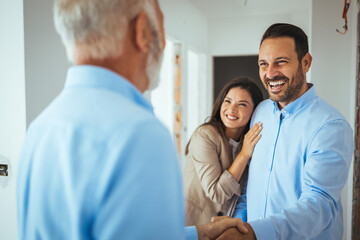 Friendly Real Estate Agent and young couple shaking hands standing in hallway, real estate agent handshaking clients at meeting, showing selling buying property for rent sale