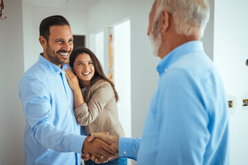Friendly Real Estate Agent and young couple shaking hands standing in hallway, real estate agent...
