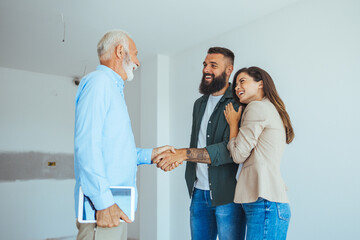 Friendly Real Estate Agent and young couple shaking hands standing in hallway, real estate agent...