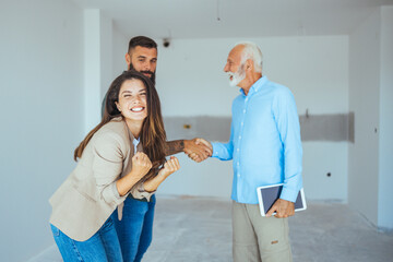 Obraz premium Real Estate Agent showing a house under construction to a couple and greeting them with a handshake at a construction site. Estate Agent Greeting Couple During Visit To New Home