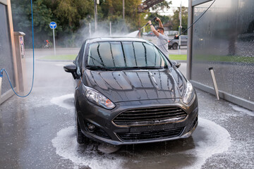 The front of a washed car, with a man washing the car in the background. A car at a self service...