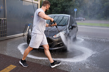 A man stands in front of the car and points a water cannon at it, washing the water off of it. A...