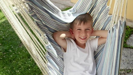 A joyful, smiling boy swings and relaxes in a garden hammock, encapsulating the essence of summertime, a carefree childhood, and the joys of vacation.