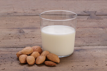 almond milk inside a glass cup and almonds with shell on rustic wooden table