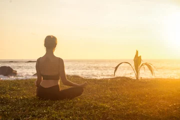 Foto op Plexiglas Rear view of slim lady meditating doing lotus yoga pose on sea beach, workout at sunset. Young woman perform sport exercises to restore strength and spirit. Healthy lifestyle concept. Copy text space © Alex Vog