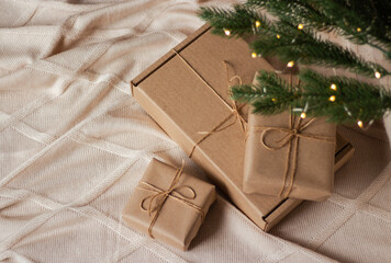 Three gift boxes in kraft wrapping paper under Christmas tree on knitted plaid. Christmas and New...