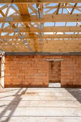 New unfinished house under construction with wooden roof beams, brick walls, concrete foundation on...