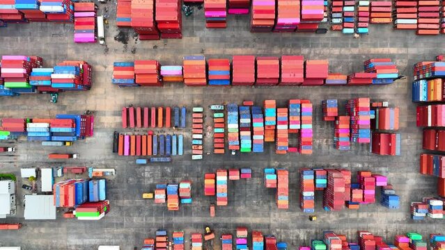 Container yard, bustling with cargo activity, seen from above by a drone, reveals orderly stacks of shipping containers and busy workers.
