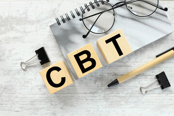 CBT Cognitive behavioral therapy concept, wooden blocks on a gray notepad with glasses