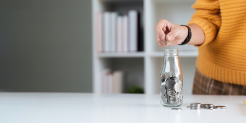hand put money coin into glass bottle for saving to save money buy a house