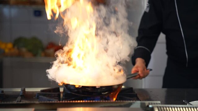 Professional chef is cooking in a frying pan in flames.