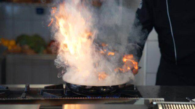 Professional chef is cooking in a frying pan in flames.