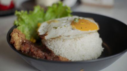 Rice bowl with sunny side up egg, chicken, vegetables and lettuce on white table in restaurant.