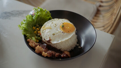 Rice bowl with sunny side up egg, chicken, vegetables and lettuce on white table in restaurant.