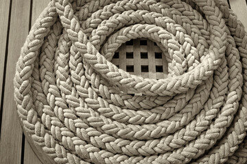On the wooden deck of the mast yacht, a white anchor rope is folded into a round bug.