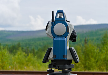 tachymeter making geodetic survey with summer forest at the background - obrazy, fototapety, plakaty