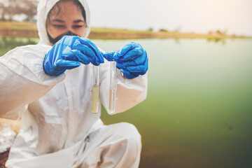 Scientist with protective suit holding a test tube with sample water in her hand. Water pollution examine concept	