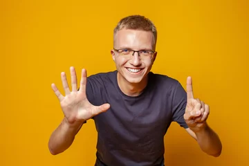 Fotobehang Happy man showing fingers number six on bright orange studio wall background © artmim