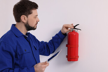 Man with tablet checking fire extinguisher indoors - obrazy, fototapety, plakaty