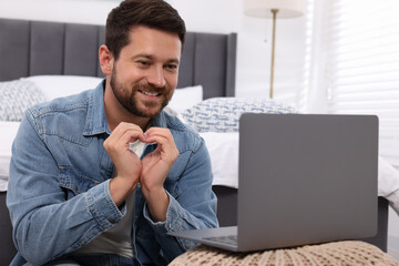 Happy man making heart with hands during video chat via laptop at home. Long-distance relationship