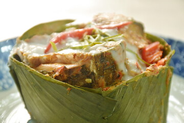 steamed chop snakehead fish with curry dressing coconut milk and topping slice lemon grass leaf in banana leaf tray on plate