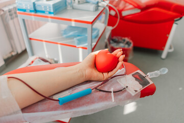 Young woman making blood donation in hospital. A woman donates blood while holding a red heart....