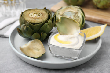 Delicious cooked artichokes with tasty sauce served on grey table, closeup