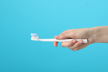 Woman holding toothbrush with paste on light blue background, closeup
