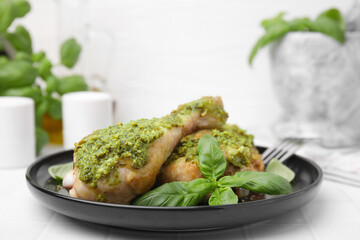 Delicious fried chicken drumsticks with pesto sauce and basil on white table, closeup