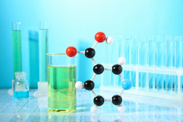 Molecular model and laboratory glassware against light blue background