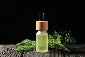 Bottle of essential oil and fresh dill on dark wooden table against black background, closeup