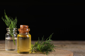Bottles of essential oil and fresh dill on wooden table against black background. Space for text