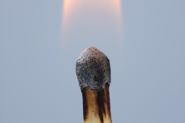 Burning match on light grey background, macro view