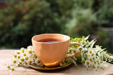 Cup of delicious chamomile tea and fresh flowers outdoors on sunny day