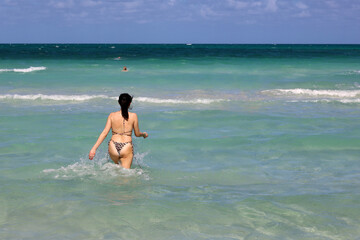 Woman in bikini running in azure sea water. Beach vacation on sunny coast